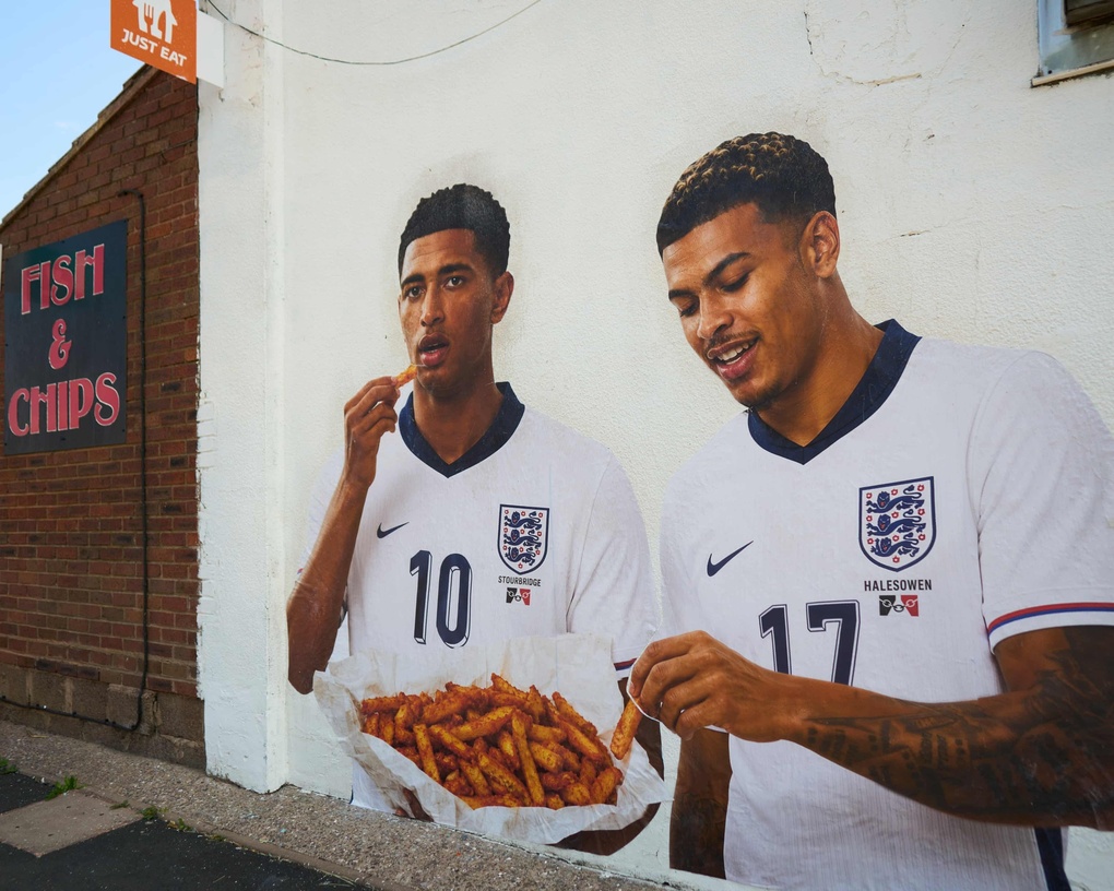 Tranh Jude Bellingham và Morgan Rogers thưởng thức món khoai tây chiên màu cam bên hông quán cá và khoai chiên ở Quinton, ngoại ô Birmingham. Ảnh: Guardian