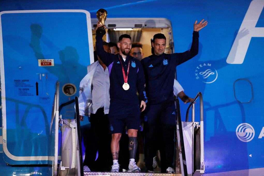 Lionnel Messi gương cao cúp vàng cùng HLV Lionel Scaloni vẫy tay chào khi tuyển Argentina hạ cánh xuống phi trường Ezeiza, Buenos Aires ngày 20/12/2022, sau chức vô địch World Cup 2022. Ảnh: Reuters